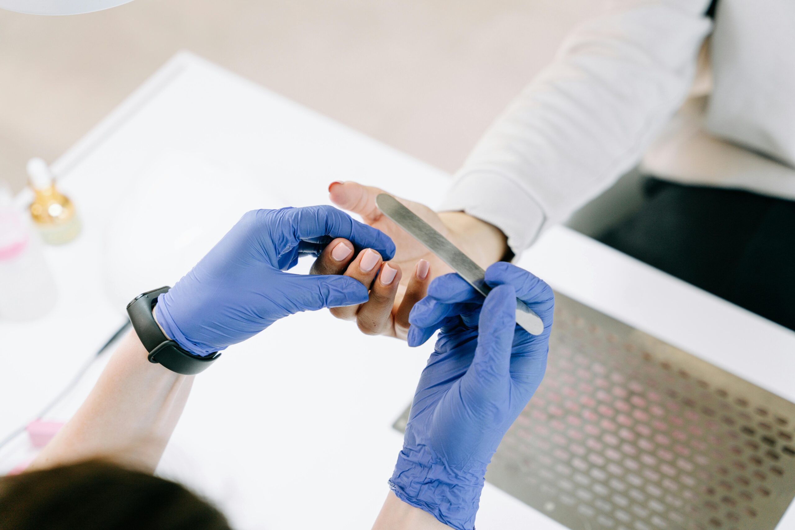 Close-up of a nail technician filing a client's nails with blue gloves in a professional setting.